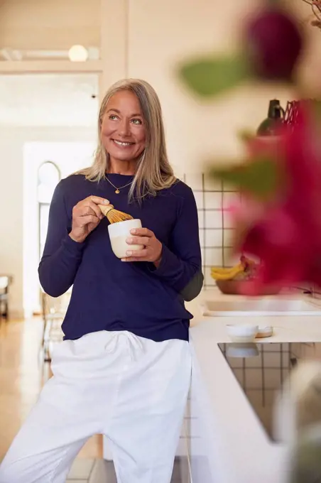 Smiling woman mixing tea by kitchen counter