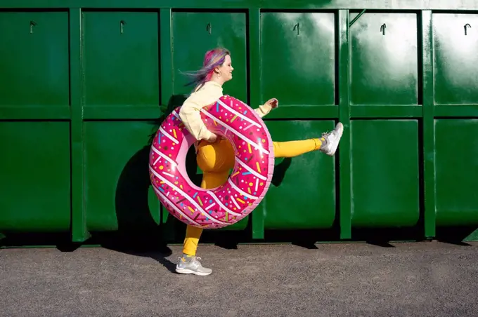 Young woman with dyed hair and floating tyre walking in front of green container