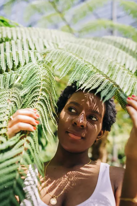 Beautiful woman hiding behind leaves at park