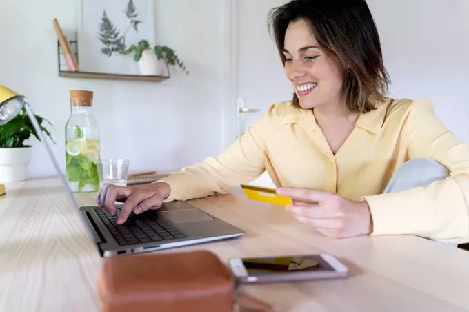 Smiling beautiful young woman enjoying online shopping through laptop at home