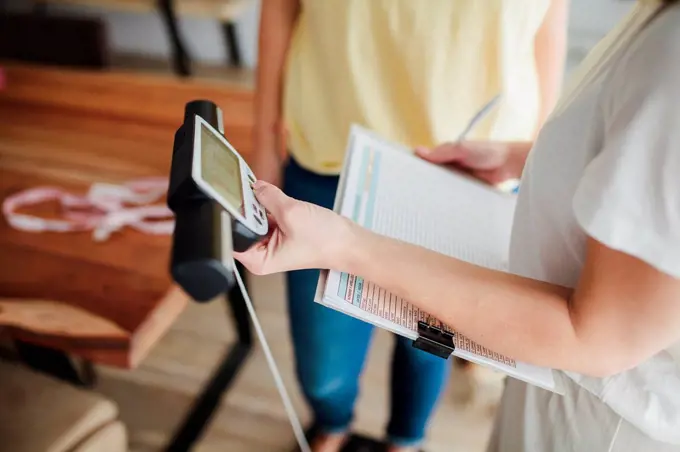 Young woman making diet plan by measuring friend's weight at home