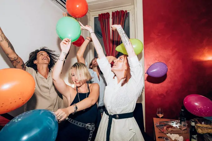 Male and female friends dancing with colorful balloons during party