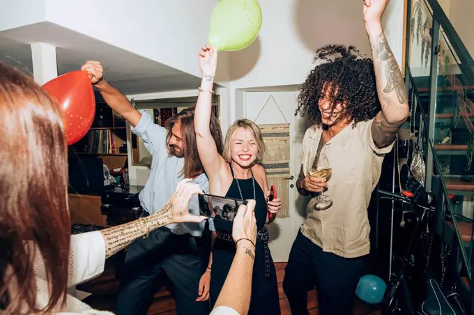 Woman photographing happy friends dancing during social gathering at home