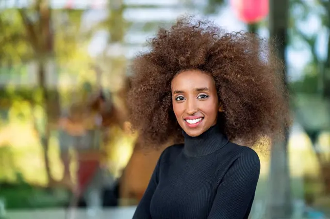 Close-up portrait of smiling businesswoman with curly frizzy hair standing outdoors