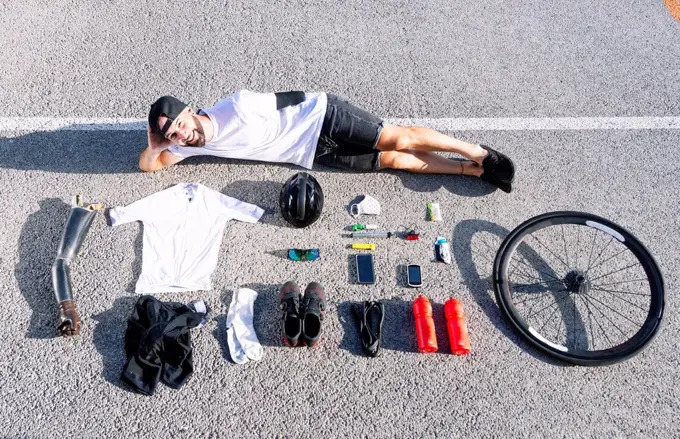 Smiling male adaptive athlete with various objects lying on road