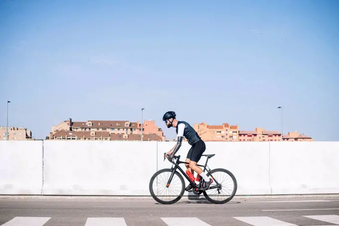 Male amputee cyclist riding bicycle on road against clear blue sky during sunny day