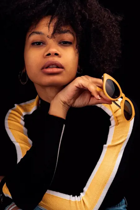 Young woman posing while holding sunglasses against black background