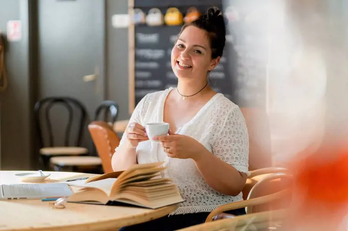 Smiling voluptuous woman holding coffee cup while sitting at table in restaurant