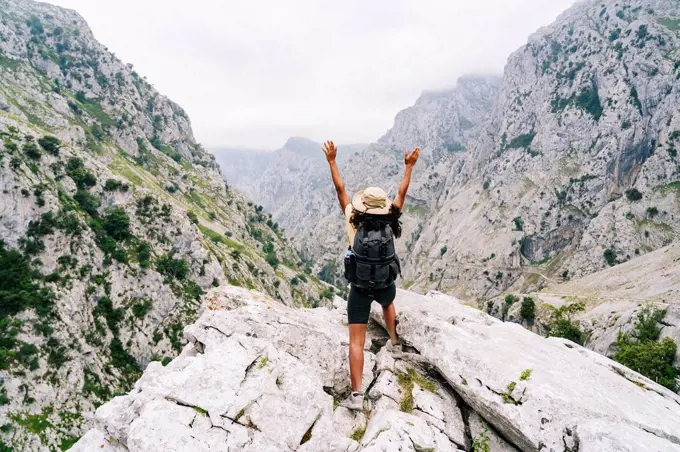 Carefree woman with hand raised standing on mountain peak at Ruta Del Cares, Asturias, Spain