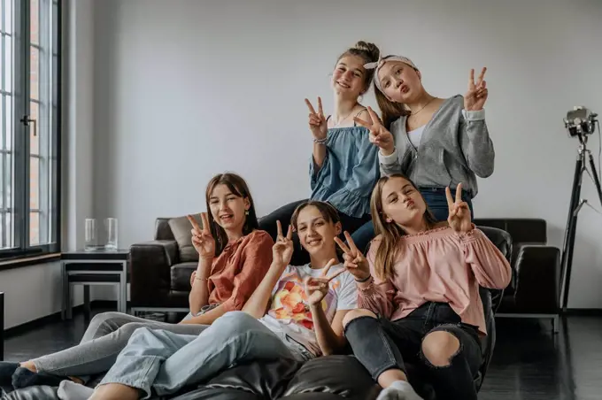 Smiling friends showing victory sign while sitting on sofa in loft apartment