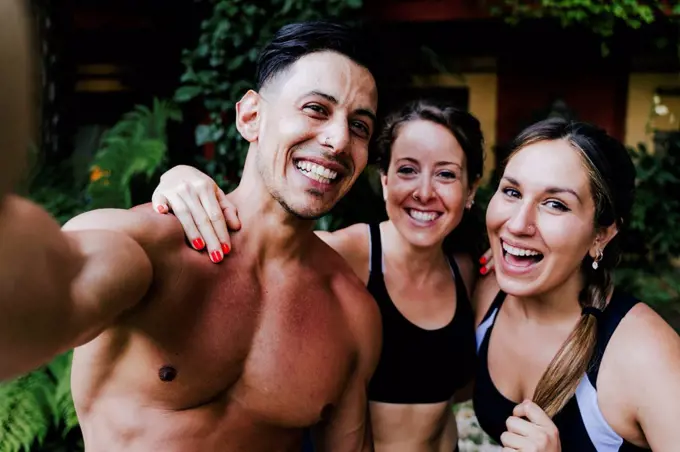 Close-up of shirtless man with cheerful female friends standing in yard