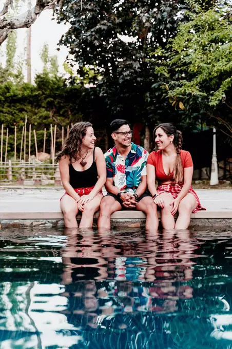 Smiling friends talking while sitting by poolside