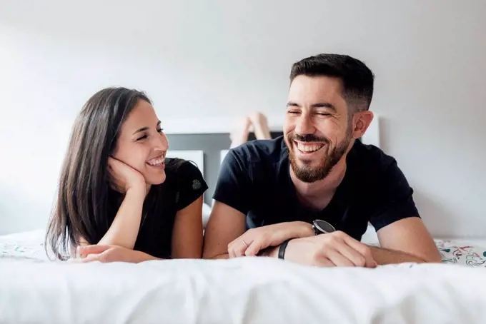 Romantic smiling couple lying on front in bedroom at home