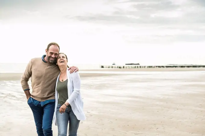 Cheerful couple laughing while walking against sea during sunset