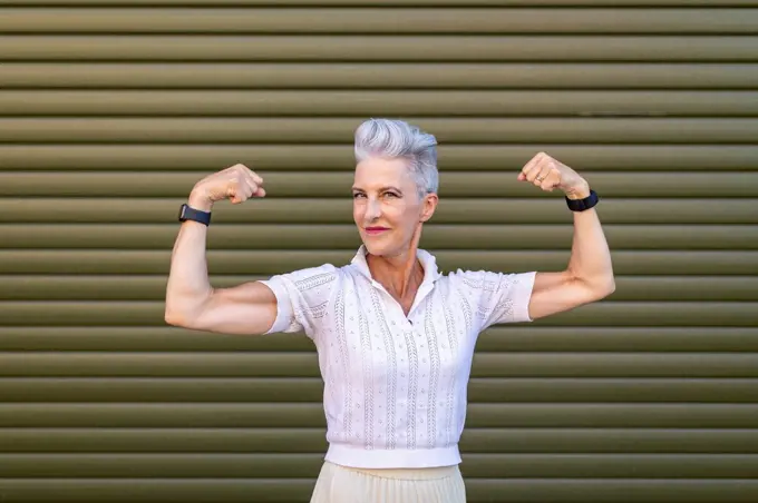 Senior woman flexing muscles while standing against shutter