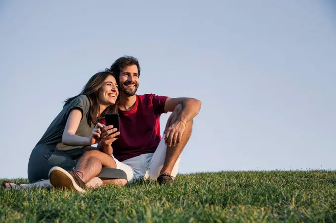 Couple sitting on grass against clear sky during sunset