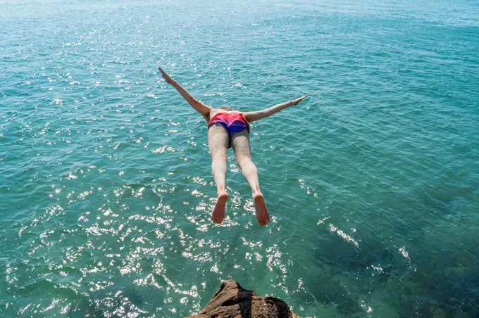 Mid adult man jumping into sea on sunny day