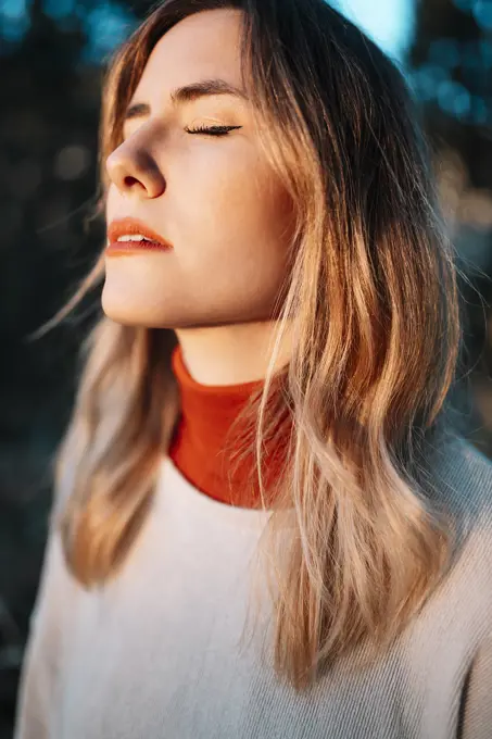 Young woman standing with eyes closed during sunset