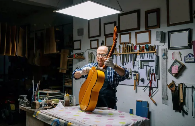 Man holding guitar on workbench while working at workshop