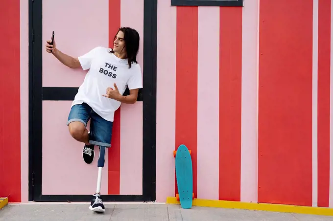 Disabled man taking selfie while standing against red wall