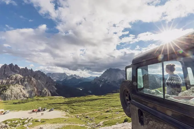 Female tourist looking at famous Dolomites while standing by car against sky during sunset, Sesto Dolomites, Alto Adige, Italy