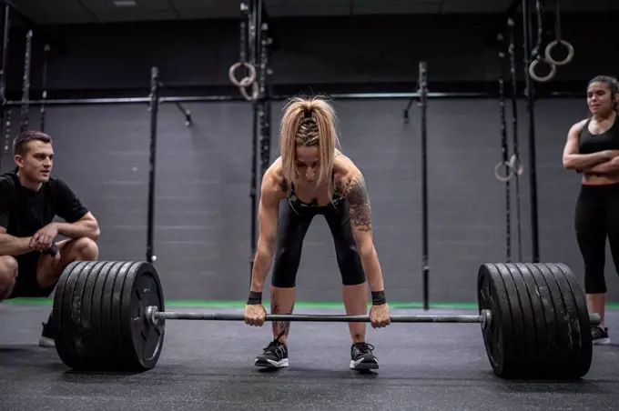 Athletes watching woman picking barbell while standing in gym