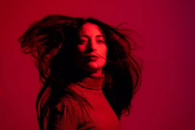 Mid adult woman staring while tossing hair against red background