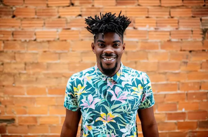 Smiling mid adult man with locs standing against brick wall in city