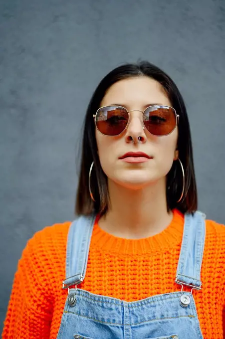 Young woman wearing sunglasses standing against gray wall