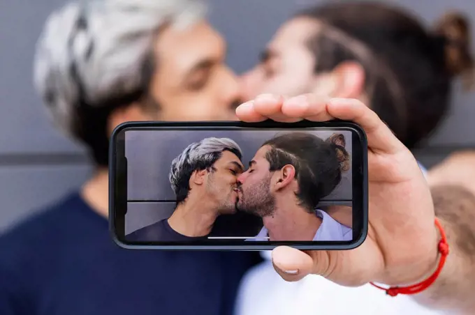 Man photographing while kissing gay partner in city