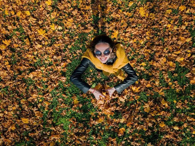 Happy woman holding dry leaves while enjoying at park during autumn