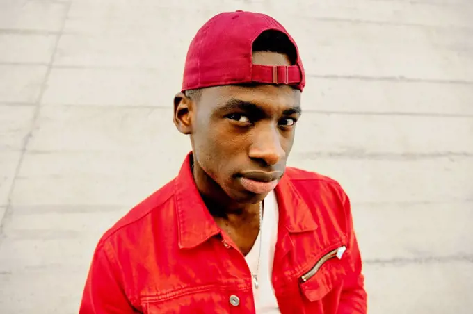 Portrait of young man in red jacket and baseball cap against concrete wall