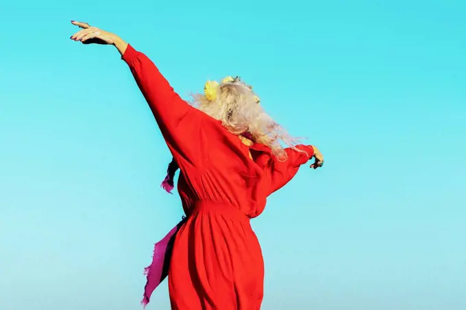 Carefree woman with arms outstretched against blue sky on sunny day