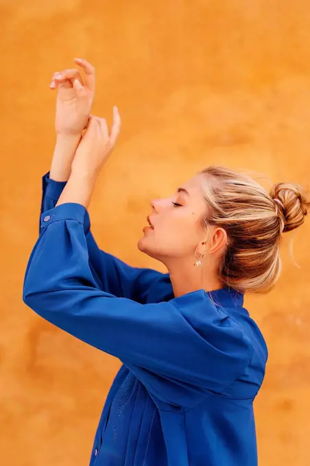 Beautiful blond woman dancing with hands raised in front of yellow wall