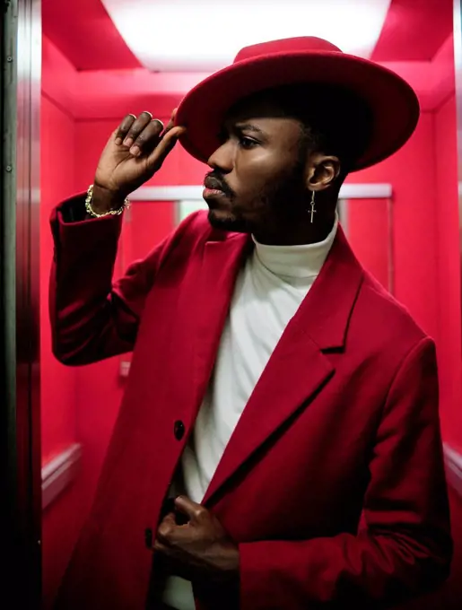 African fashionable man holding hat while peeking outside elevator