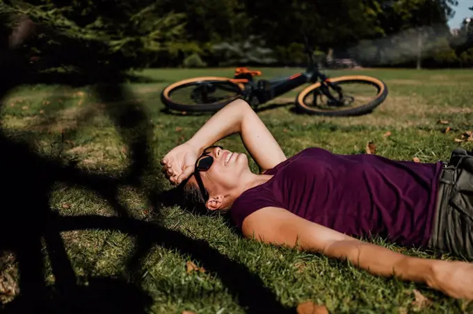 Woman lying on grass while resting by mountain bike at park