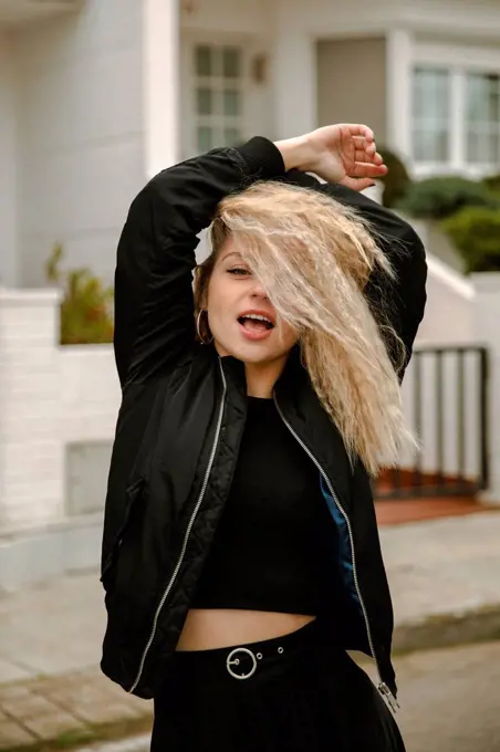 Blond hipster woman with arms raised standing on street