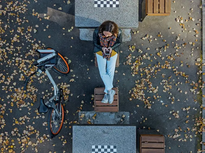 Woman using smart phone while sitting amidst chess tables in park during autumn