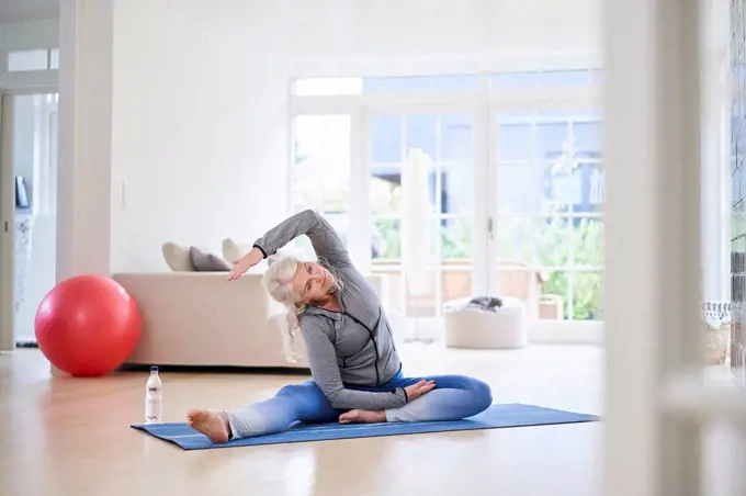 Senior woman stretching arms while exercising in living room