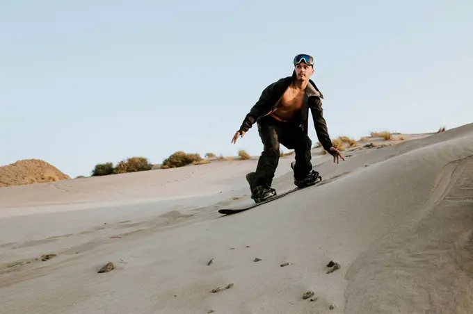 Young man looking away while sandboarding against clear sky at Almeria, Tabernas desert, Spain