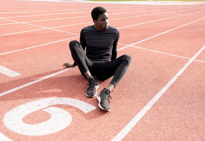 Sportsman contemplating while sitting on running track during sunny day