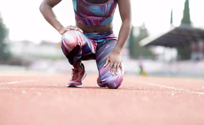 Young female sportsperson kneeling on starting line at running track