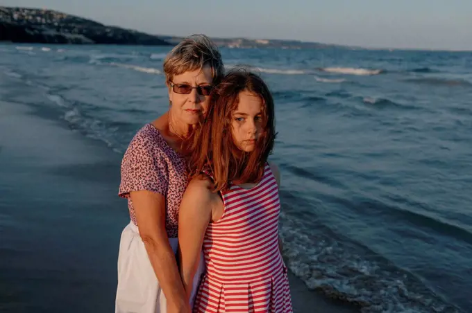 Granddaughter standing with grandmother by water at beach