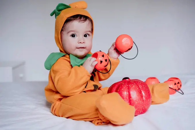 Baby boy wearing halloween costume playing with pumpkin toy sitting at home