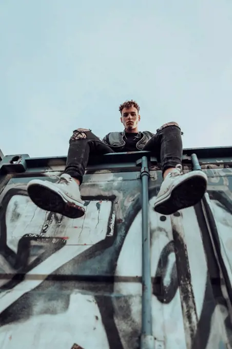 Fashionable young man on metal container against sky