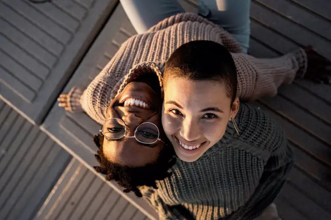 Smiling friends leaning on each other shoulder while sitting on bench