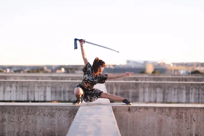 Young female athlete practicing sword on structure against clear sky during sunset