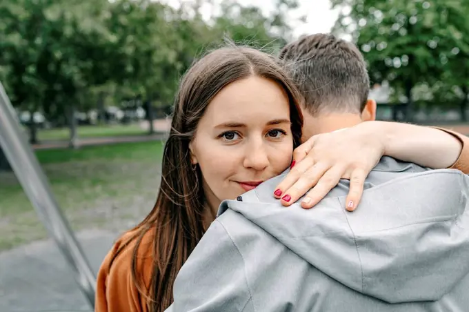 Smiling girlfriend embracing boyfriend in public park