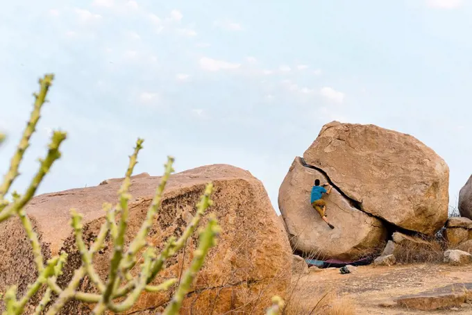 Determinant young man boulderer climbing rock, Karnataka, Hampi, India