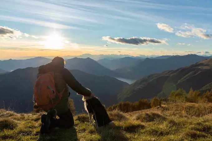 Hiker kneeling while stroking dog at mountain peak during sunset